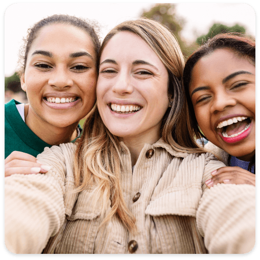 Three women smiling and taking a selfie, showcasing their bright smiles