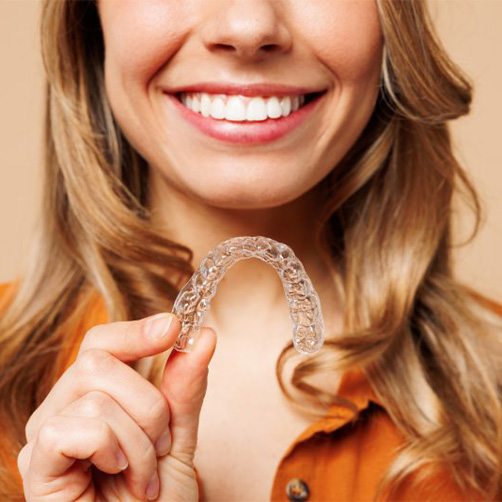 Woman smiling and holding an Invisalign tray